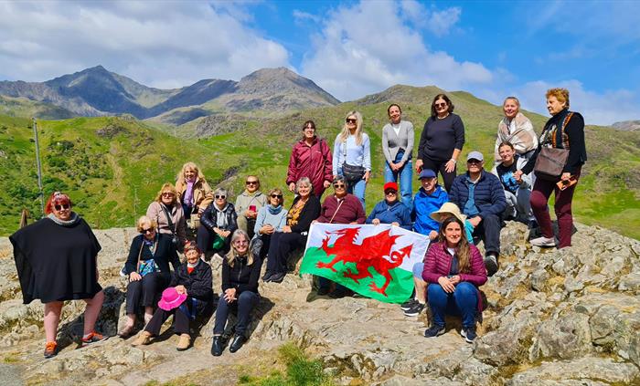 A group of people holding a Welsh flag on a mountain.